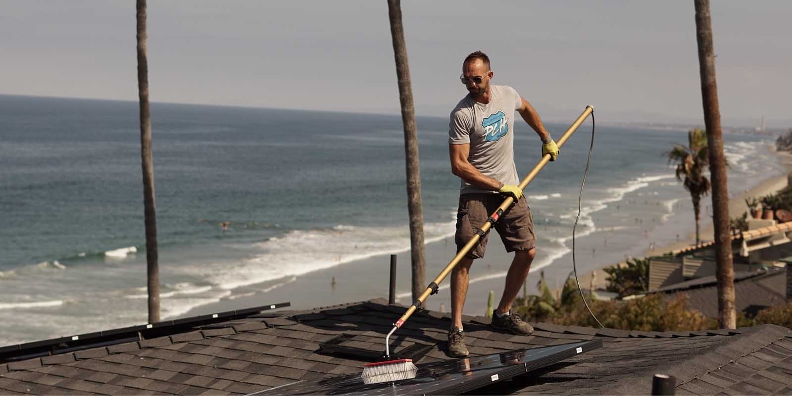 Aaron brushing rooftop solar panels clean above the surf in North County San Diego