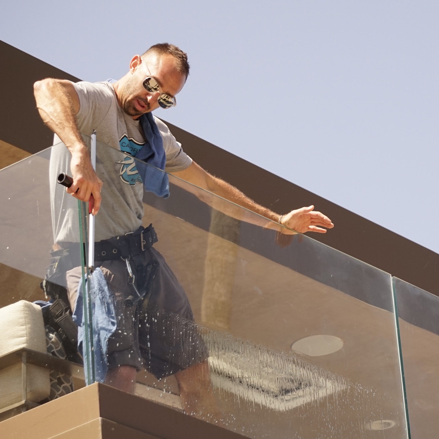 Aaron of PCH Services cleaning a glass balcony railing on a North County home